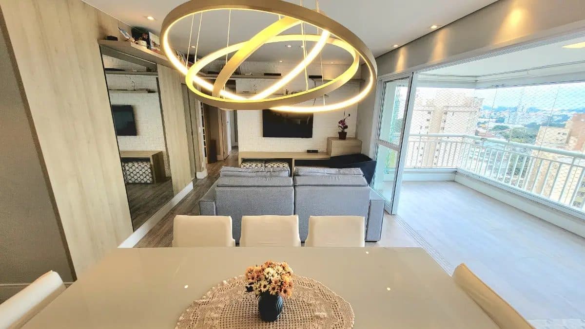 Sala de estar com sofá cinza, parede de tijolinhos brancos, TV e acesso à varanda envidraçada.